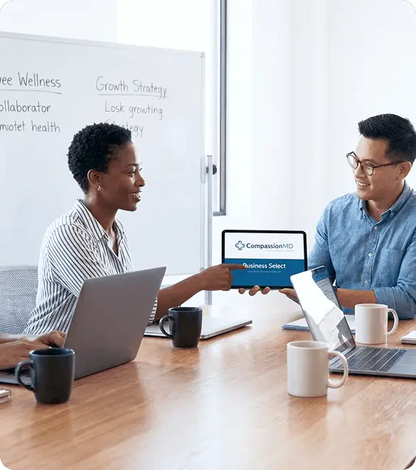 One male and one female sitting on a confarens room, holding a tab showing Compression MD business select option