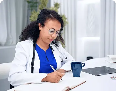 A female doctor sitting on her desk and writting something.