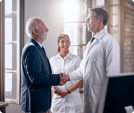 A male Doctor and a business man shaking hands and a female doctor is also standing with them smiling.