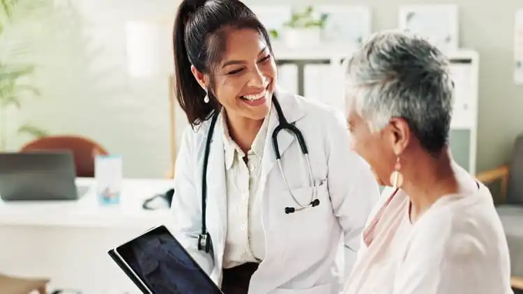 A female doctor is talking with a old women while holding a tab on her hand